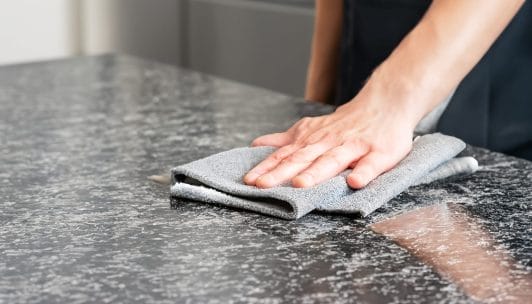 A person cleans a granite countertop following Hilltop Surfaces granite maintenance tips.